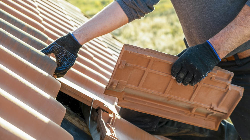 Dachreparatur Dachecker mit Dachpfanne in der Hand bei der Neueindeckung eines Daches